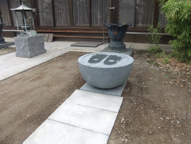 寺院境内に設置されたM1H材の仏足石。半円形の石に仏足形が刻まれ、参拝者が手を合わせる祈りの空間を演出しています。